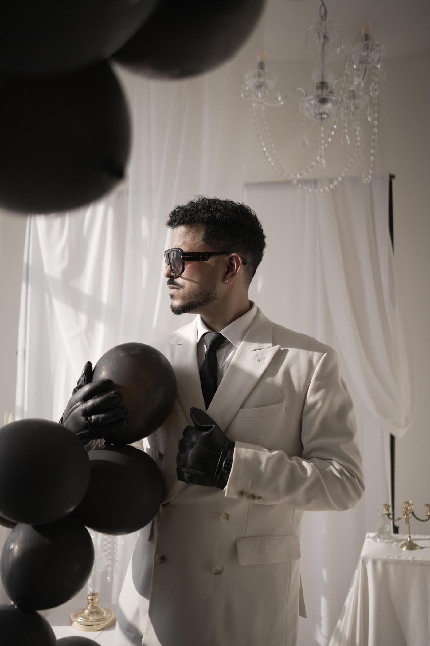 Semwal in a white suit holding black balloons beneath a chandelier